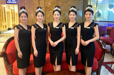 黑色礼仪制服客服人员在红色沙发前列队合影，头戴白色礼仪发饰
